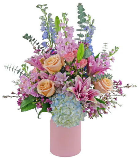 Pastels including pink, peach, blue, and lavender...featuring double lilies, shimmer roses, stock, hydrangea and much more. The vase is available in your choice of 3 colors, pink, white or green.