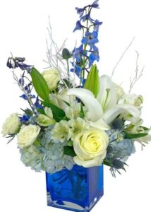 True Blue is a striking design in a blue glass cube. It is made with white lilies, roses and spray roses, blue hydrangea and delphinium. All are arranged by hand and ready for delivery today.
